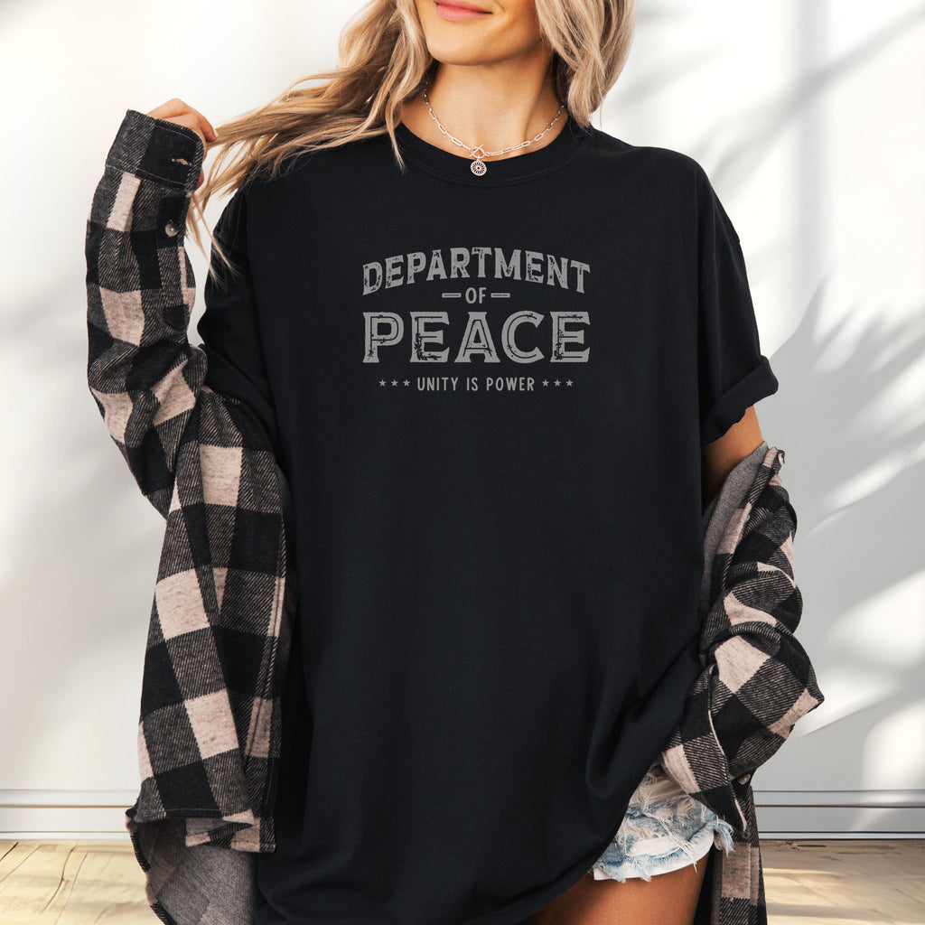Female model wearing oversized black t-shirt with distressed text reading “Department of Peace — Unity is Power” in vintage style design.