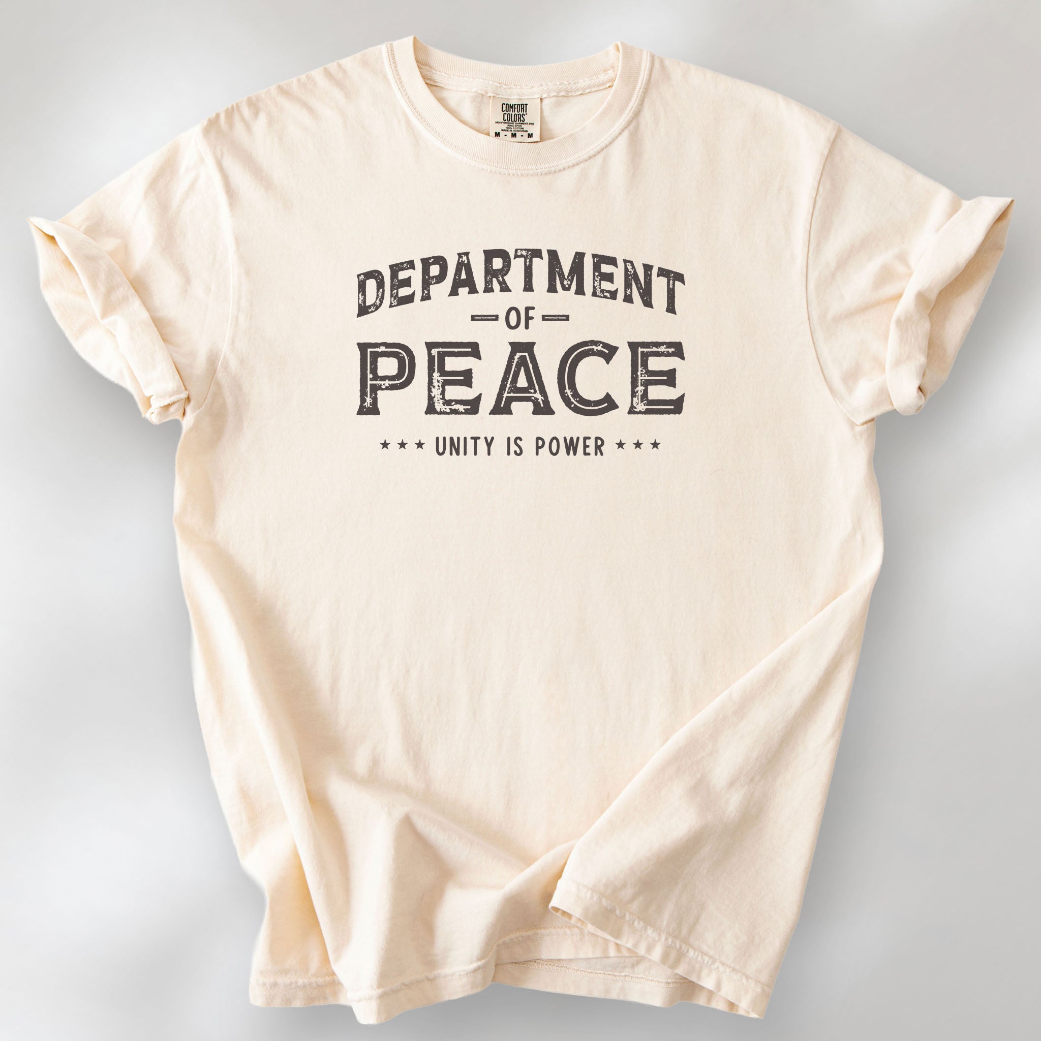Ivory t-shirt with distressed text reading “Department of Peace — Unity is Power” in vintage style design.