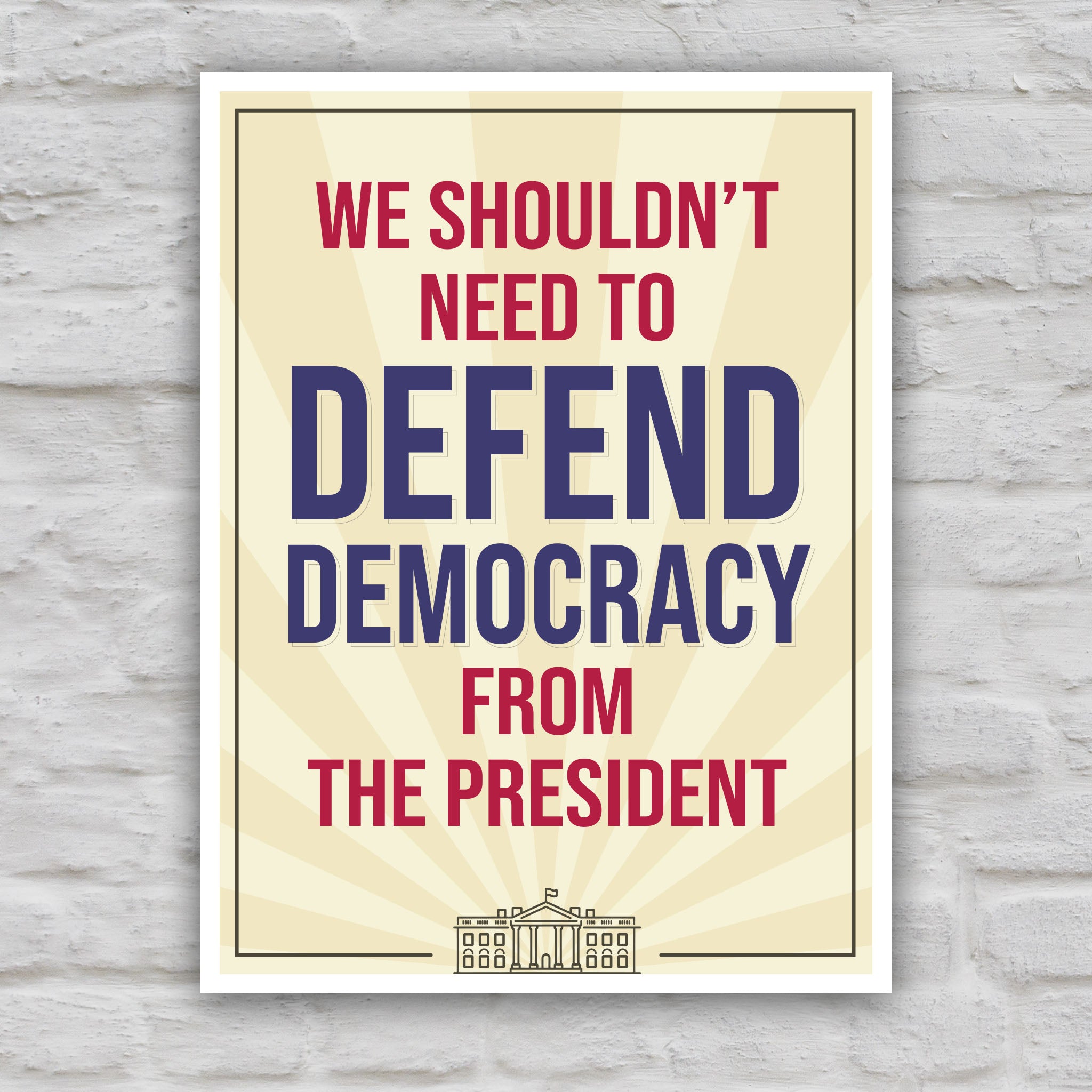 Color version of protest sign with a light gold background and red and blue text that reads "we shouldn't need to defend democracy from the president".