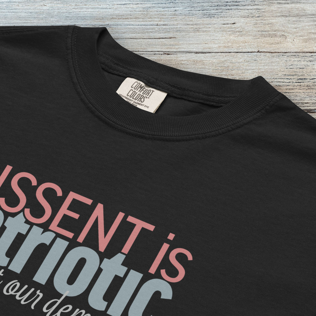 Closeup detail of black t-shirt with bold stylized red and blue text that reads "dissent is patriotic" with script text below that reads "protest our democracy".