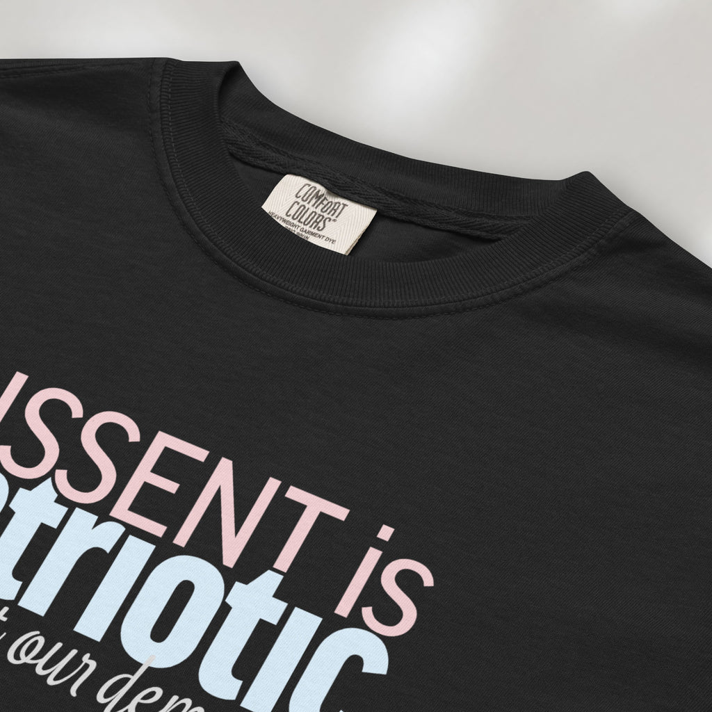 Closeup detail of black t-shirt with bold stylized red and blue text that reads "dissent is patriotic" with script text below that reads "protest our democracy".