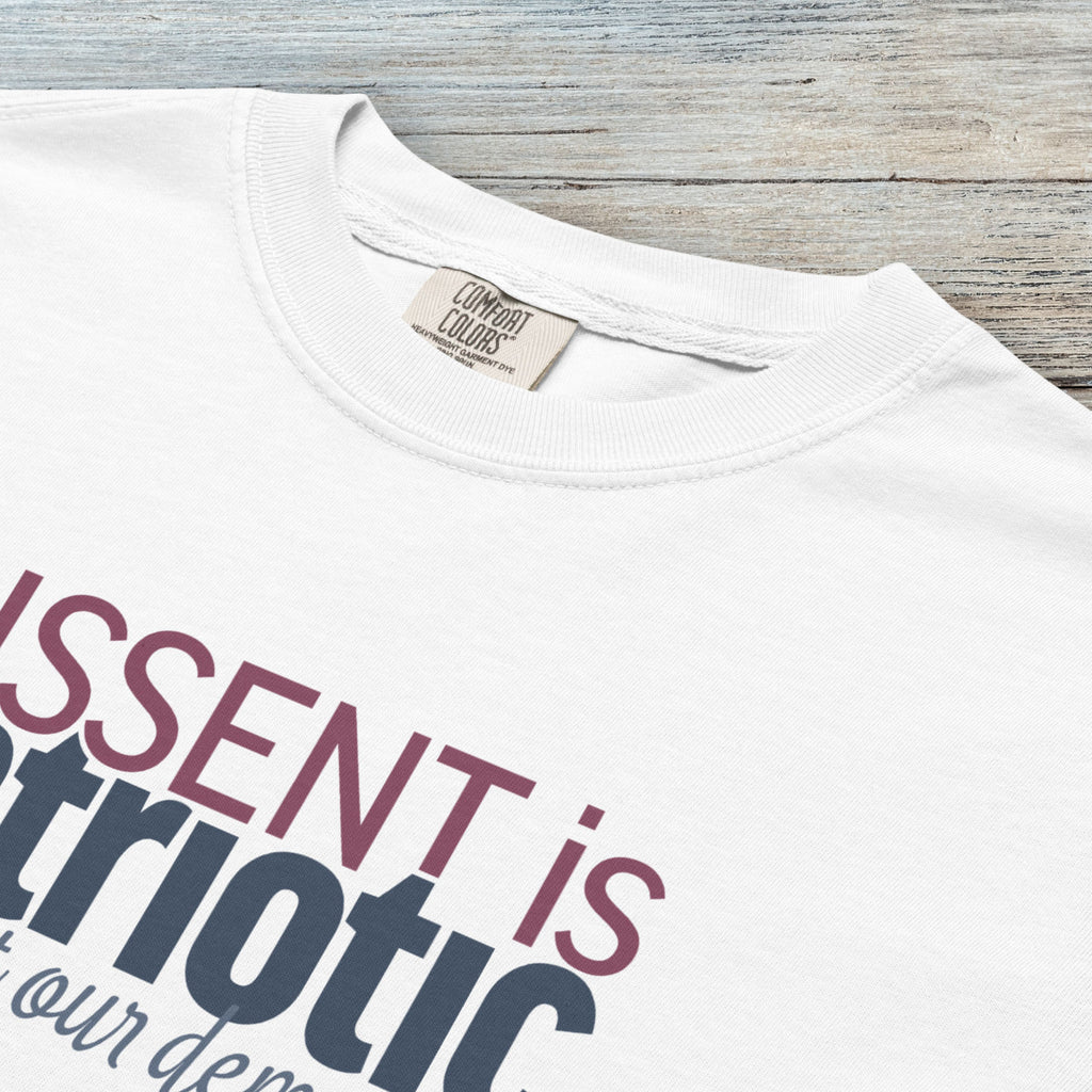 Closeup detail of white unisex t-shirt with bold text reading “Dissent is Patriotic – Protect Our Democracy” in red, blue, and gray.