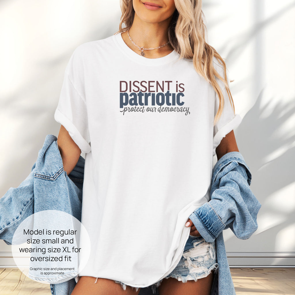Female model wearing oversized white t-shirt with bold stylized red and blue text that reads "dissent is patriotic" with script text below that reads "protest our democracy". Includes size and fit information for the model who is regular size small, and wearing a size XL shirt for an oversized fit.
