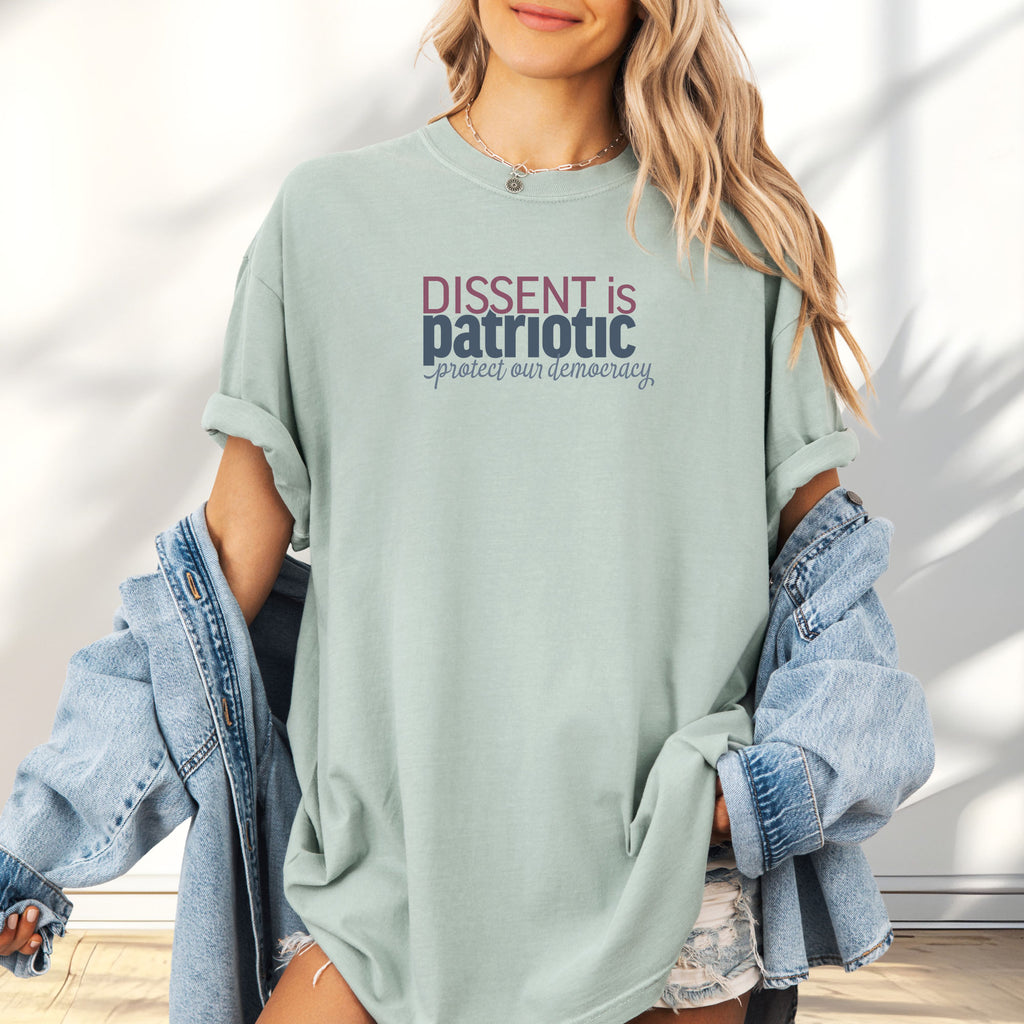 Female model wearing oversized bay unisex t-shirt with bold text reading “Dissent is Patriotic – Protect Our Democracy” in red, blue, and gray.