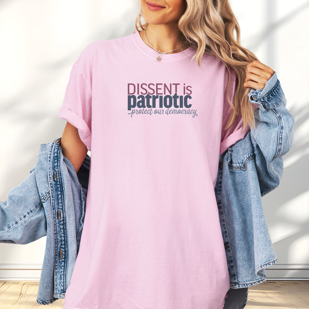 Female model wearing blossom unisex t-shirt with bold text reading “Dissent is Patriotic – Protect Our Democracy” in red, blue, and gray.