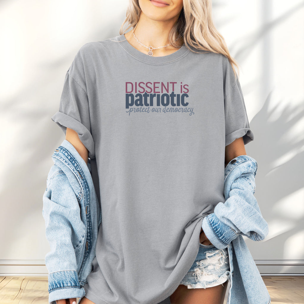 Female model wearing granite unisex t-shirt with bold text reading “Dissent is Patriotic – Protect Our Democracy” in red, blue, and gray.