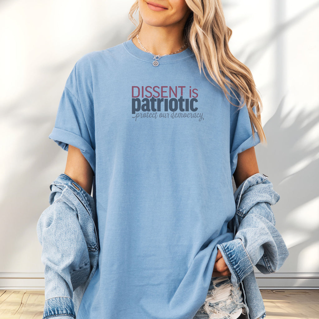 Female model wearing oversized washed denim unisex t-shirt with bold text reading “Dissent is Patriotic – Protect Our Democracy” in red, blue, and gray.