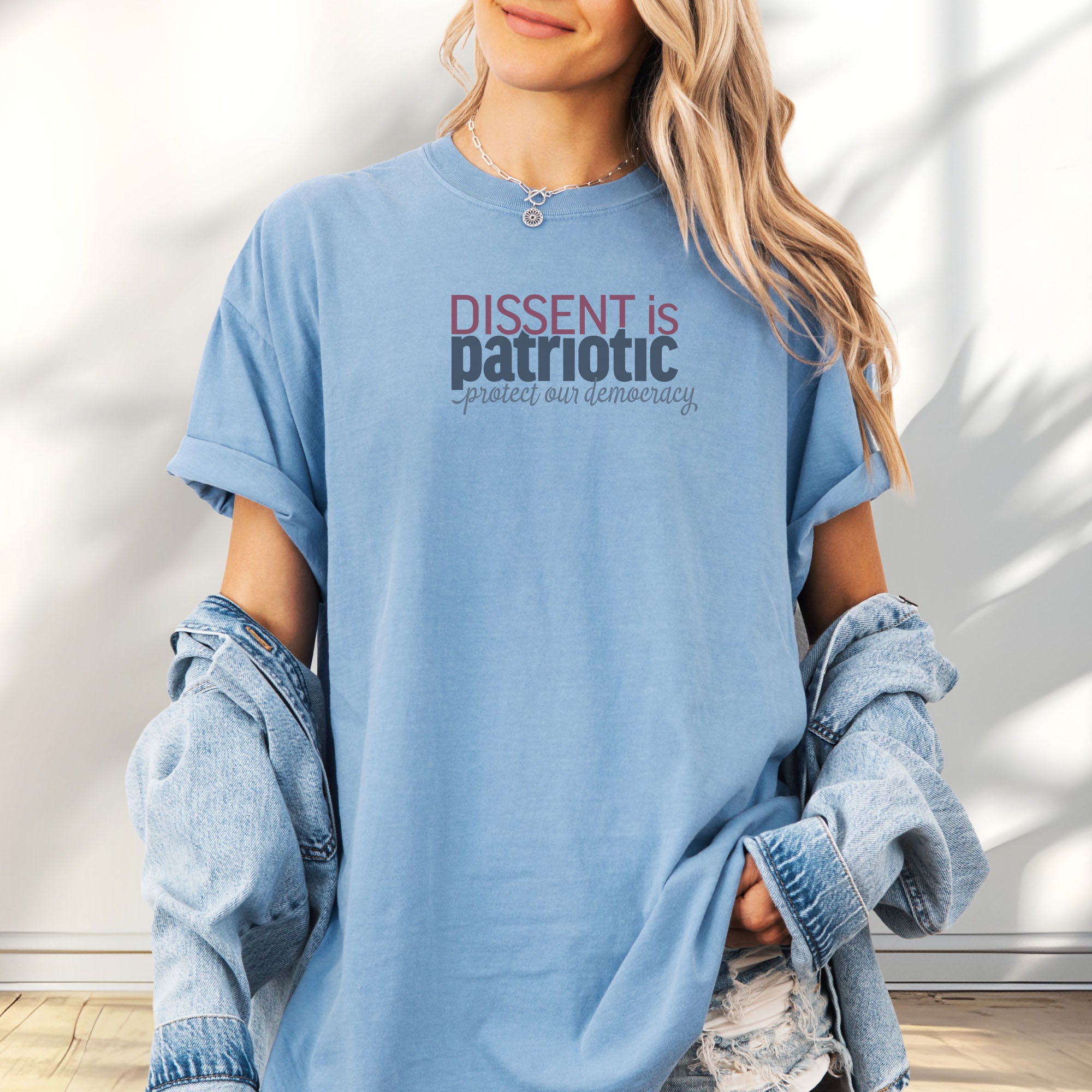 Female model wearing oversized washed denim unisex t-shirt with bold text reading “Dissent is Patriotic – Protect Our Democracy” in red, blue, and gray.