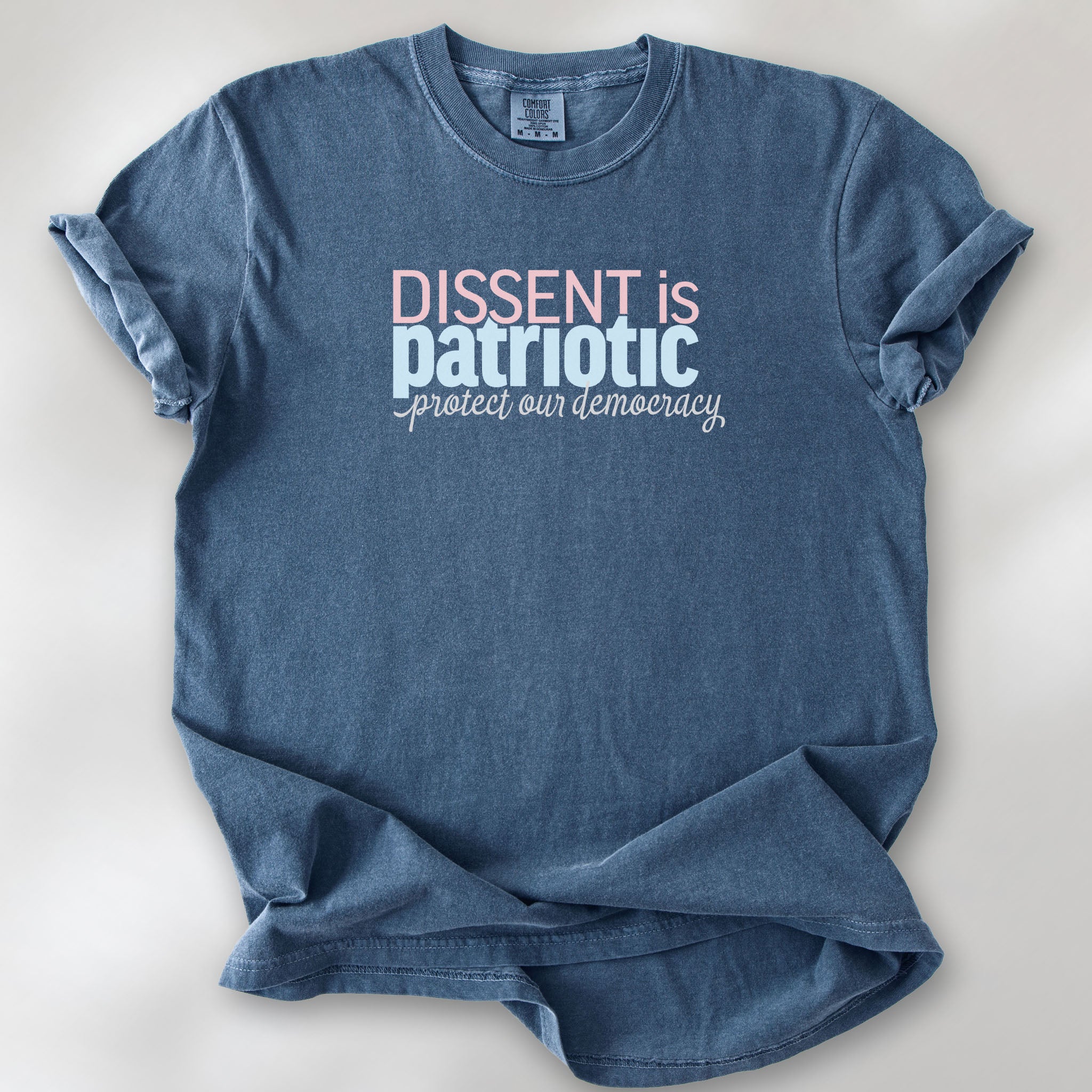 Denim t-shirt with bold stylized red and blue text that reads "dissent is patriotic" with script text below that reads "protest our democracy".