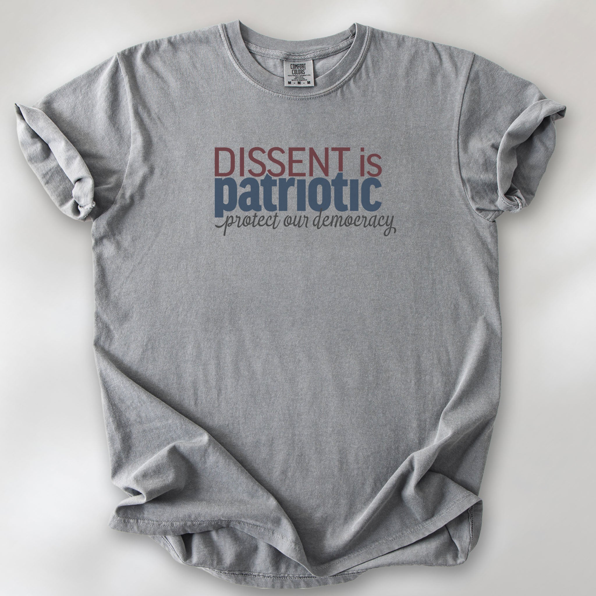 Grey t-shirt with bold stylized red and blue text that reads "dissent is patriotic" with script text below that reads "protest our democracy".