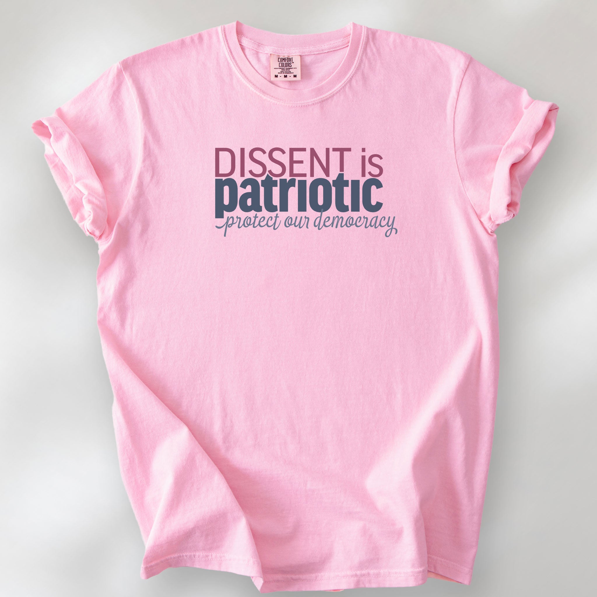 Blossom unisex t-shirt with bold text reading “Dissent is Patriotic – Protect Our Democracy” in red, blue, and gray.