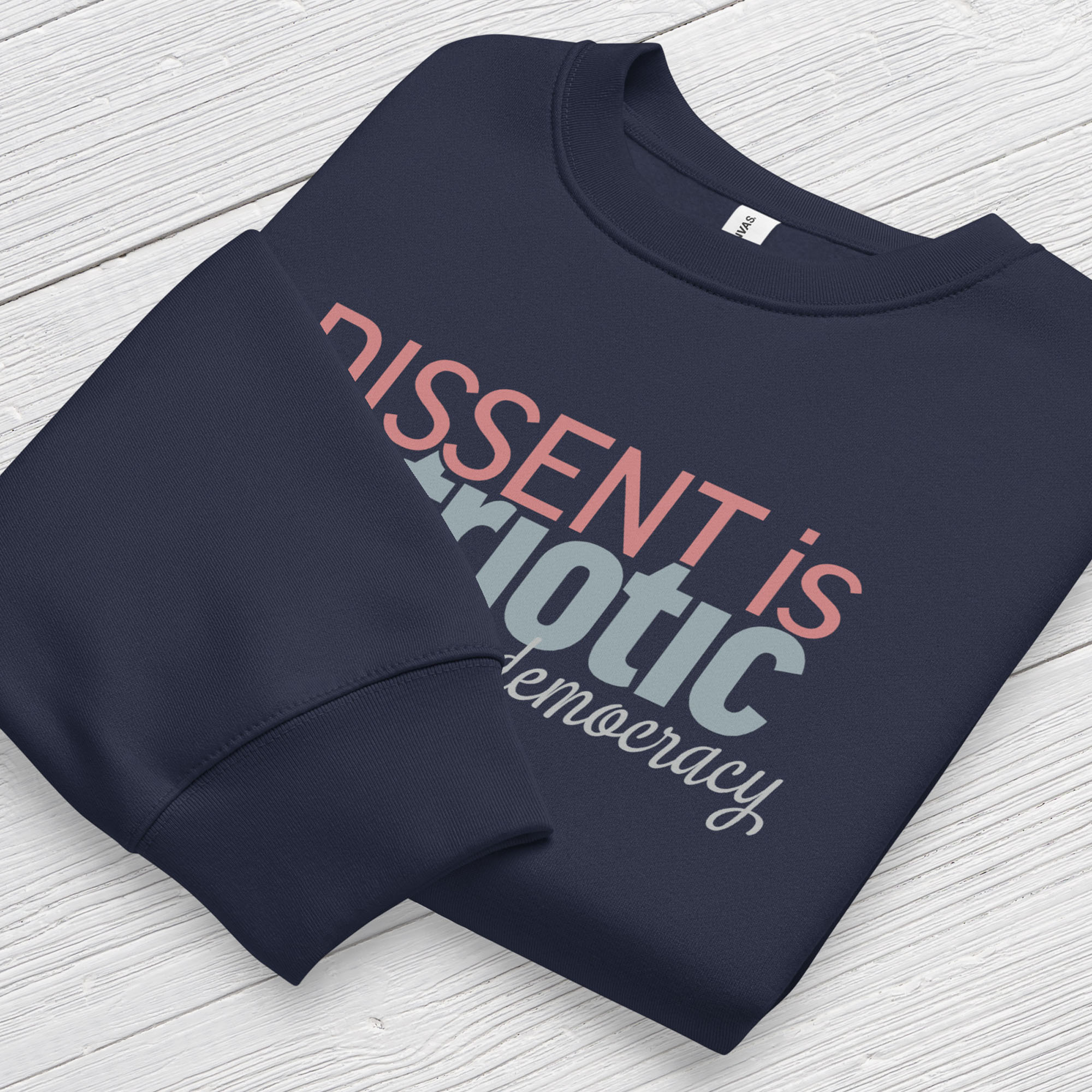 Folded navy sweatshirt with bold stylized red and blue text that reads "dissent is patriotic" with script text below that reads "protest our democracy".
