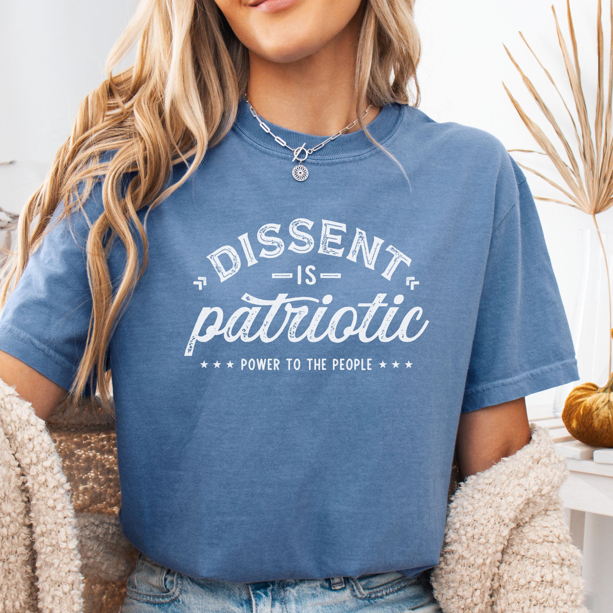 Female model wearing blue jean vintage design style shirt reading "Dissent Is Patriotic — Power To The People" in distressed typography.