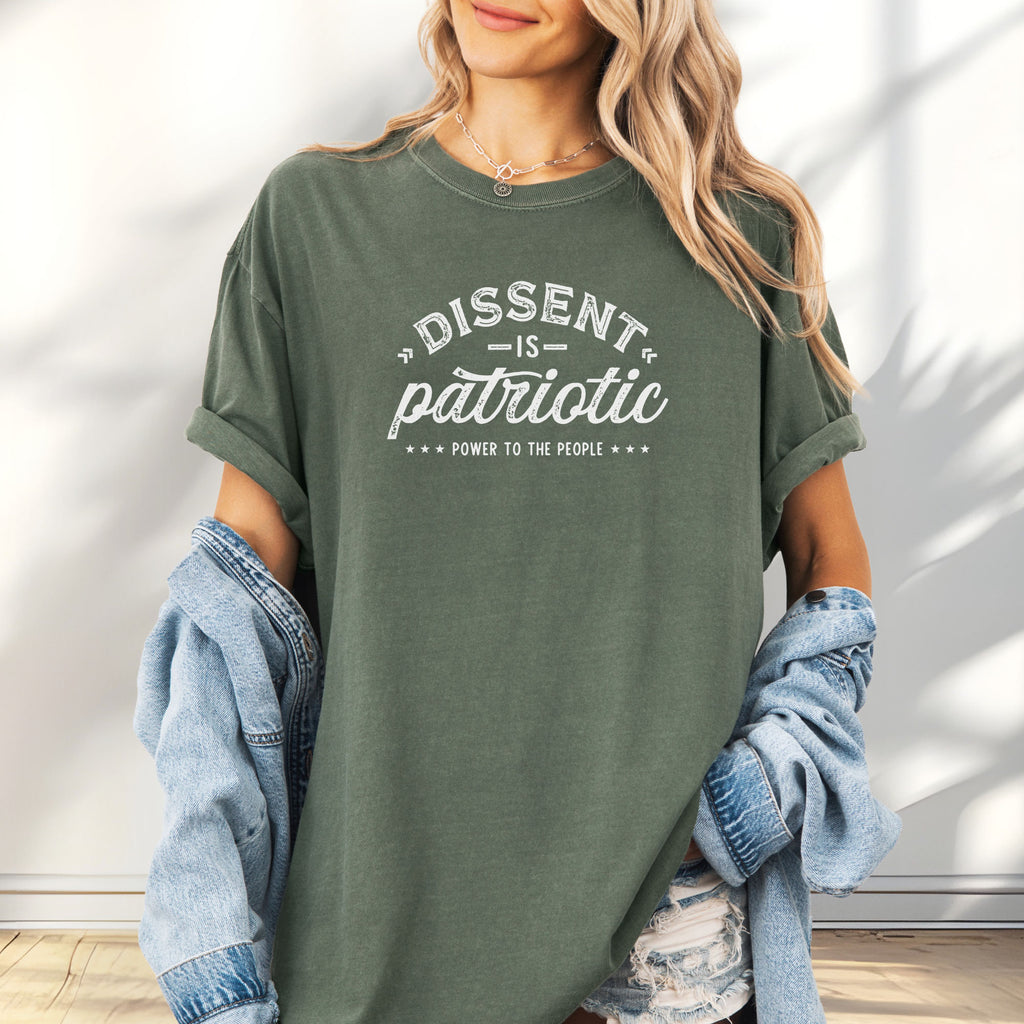 Female model wearing oversized moss vintage design style shirt reading "Dissent Is Patriotic — Power To The People" in distressed typography.