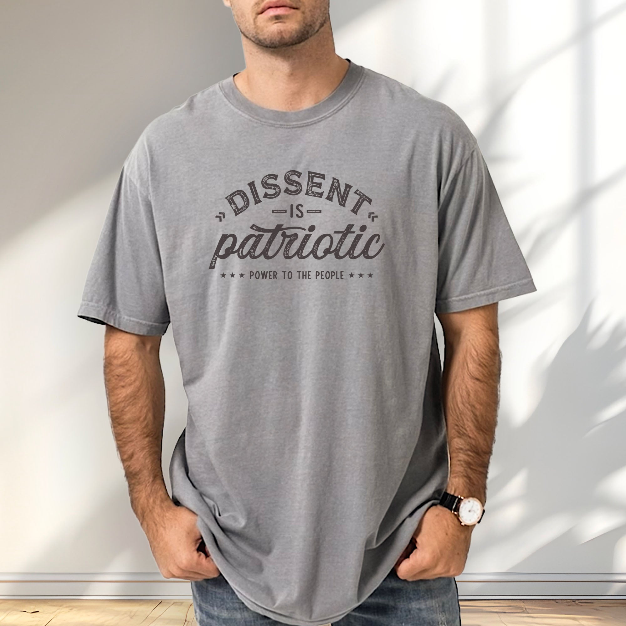 Male model wearing grey vintage design style shirt reading "Dissent Is Patriotic — Power To The People" in distressed typography.