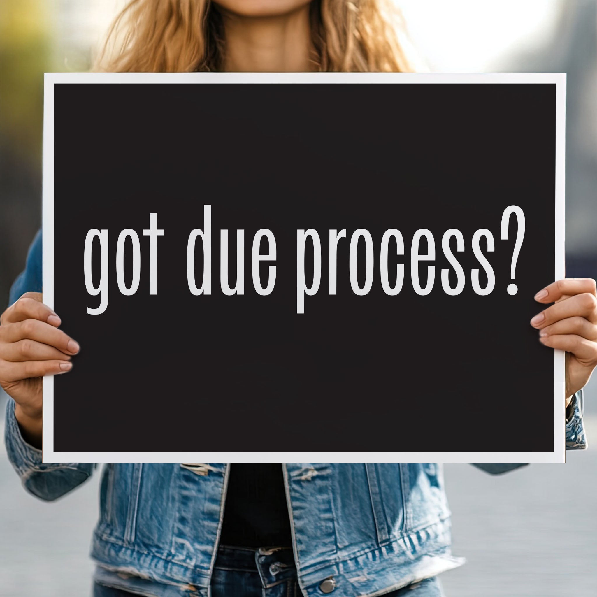Person holding protest sign with black background and bold white text that says “got due process?” in the style of the “got milk?” campaign.