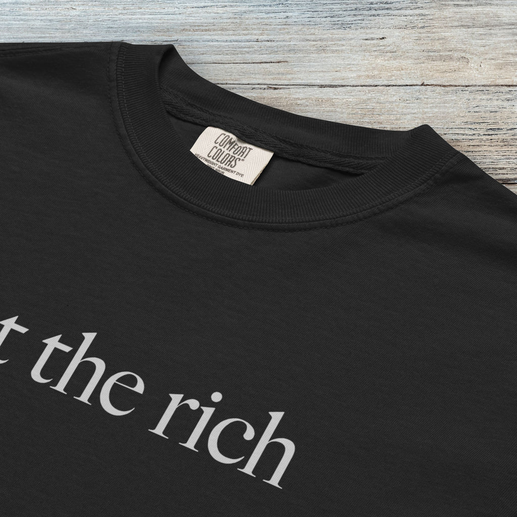 Closeup detail of black t-shirt with minimalist light grey text reading “eat the rich."