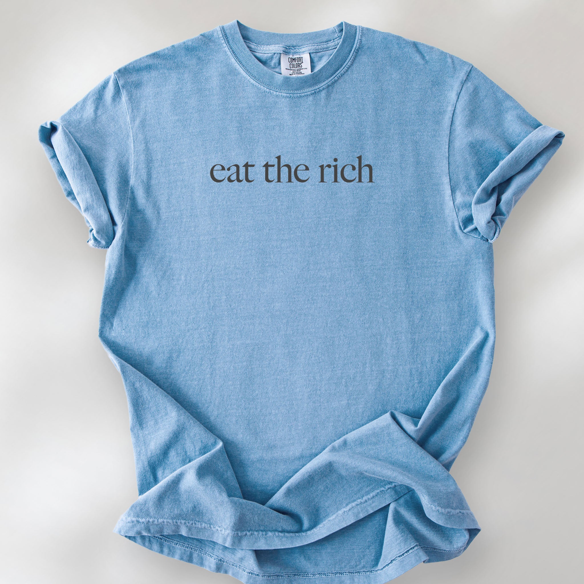 Washed denim t-shirt with minimalist dark grey text reading “eat the rich."
