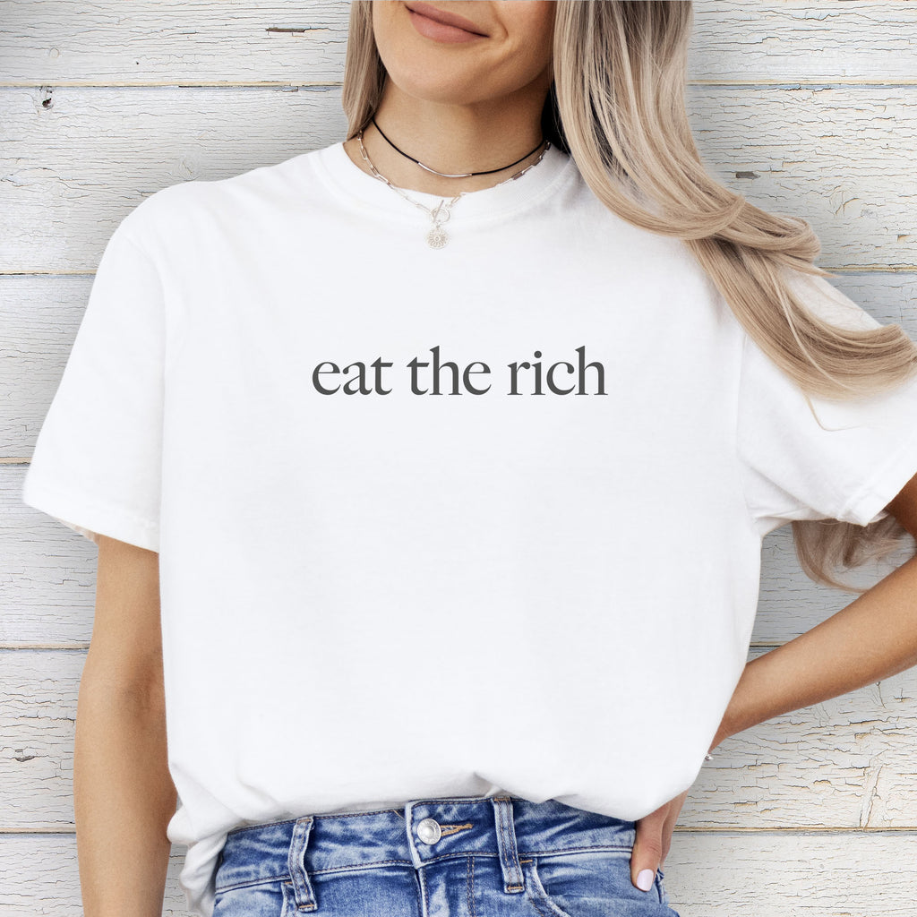 Female model wearing white t-shirt with minimalist dark grey text reading “eat the rich."