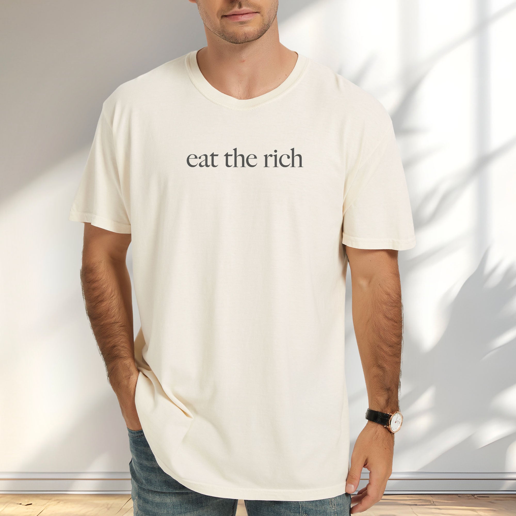 Male model wearing ivory t-shirt with minimalist dark grey text reading “eat the rich."