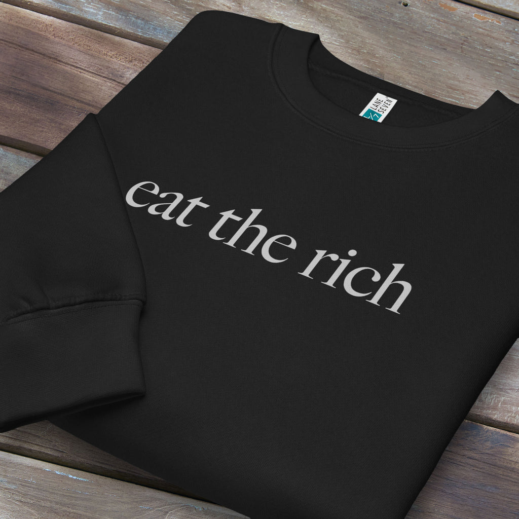 Folded black sweatshirt with minimalist light grey text reading “eat the rich."