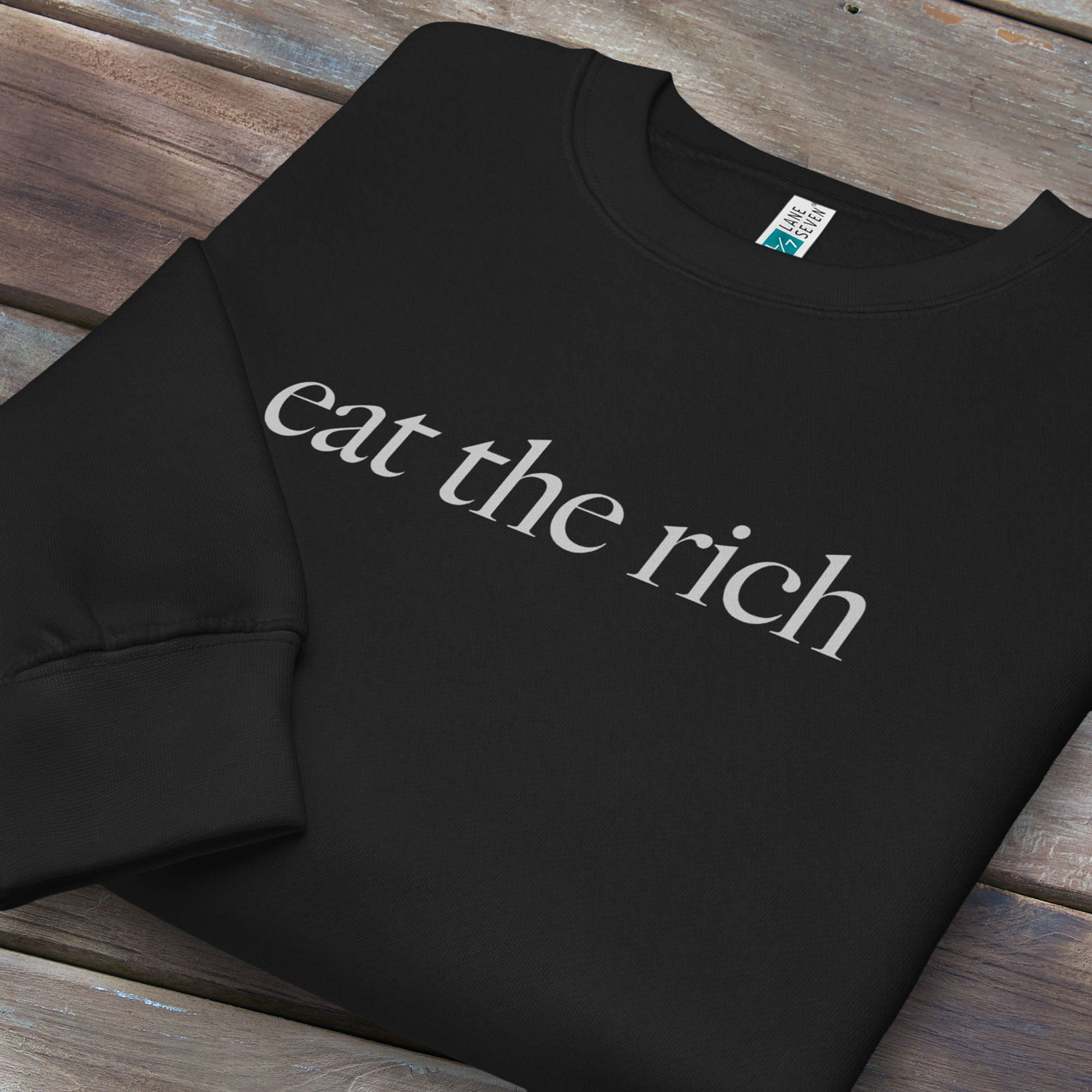 Folded black sweatshirt with minimalist light grey text reading “eat the rich."