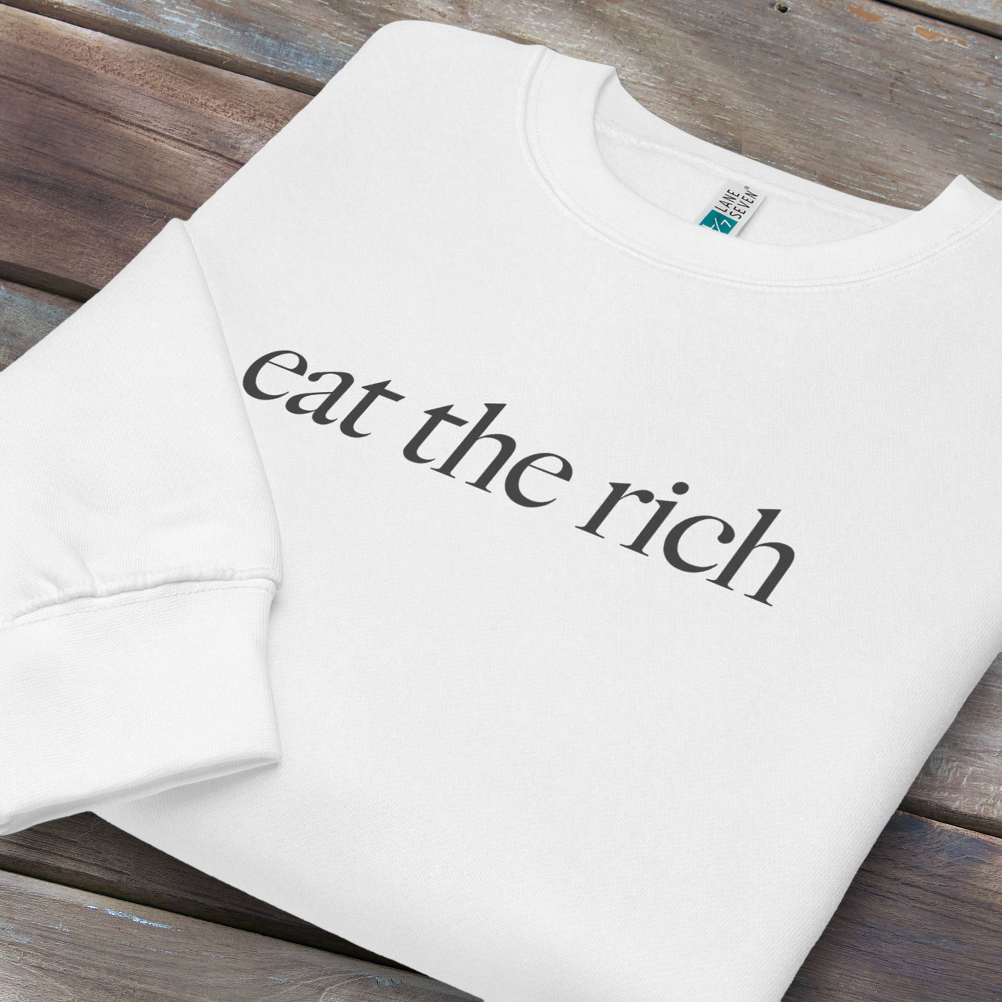 Folded white sweatshirt with minimalist dark grey text reading “eat the rich."