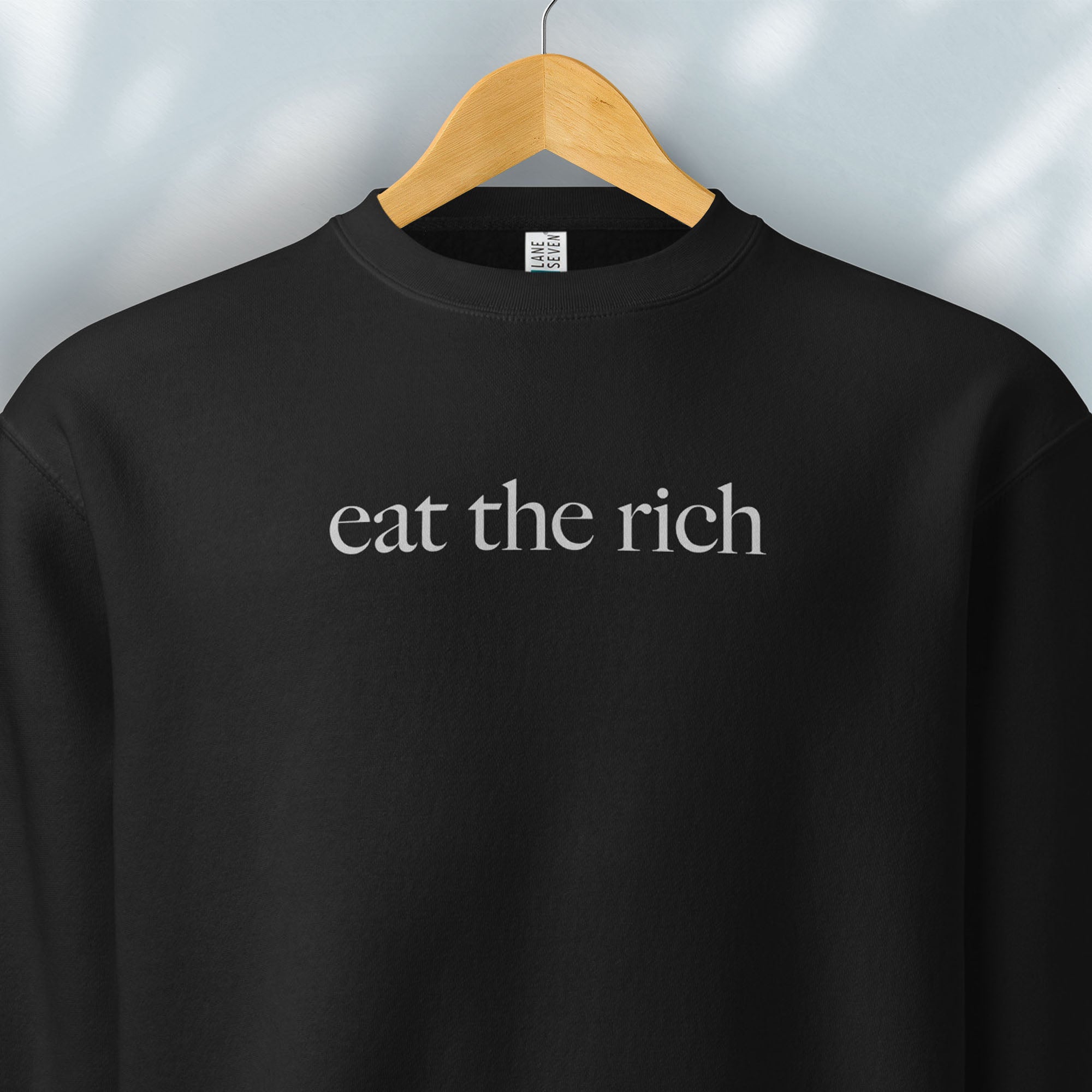 Hanging black sweatshirt with minimalist light grey text reading “eat the rich."