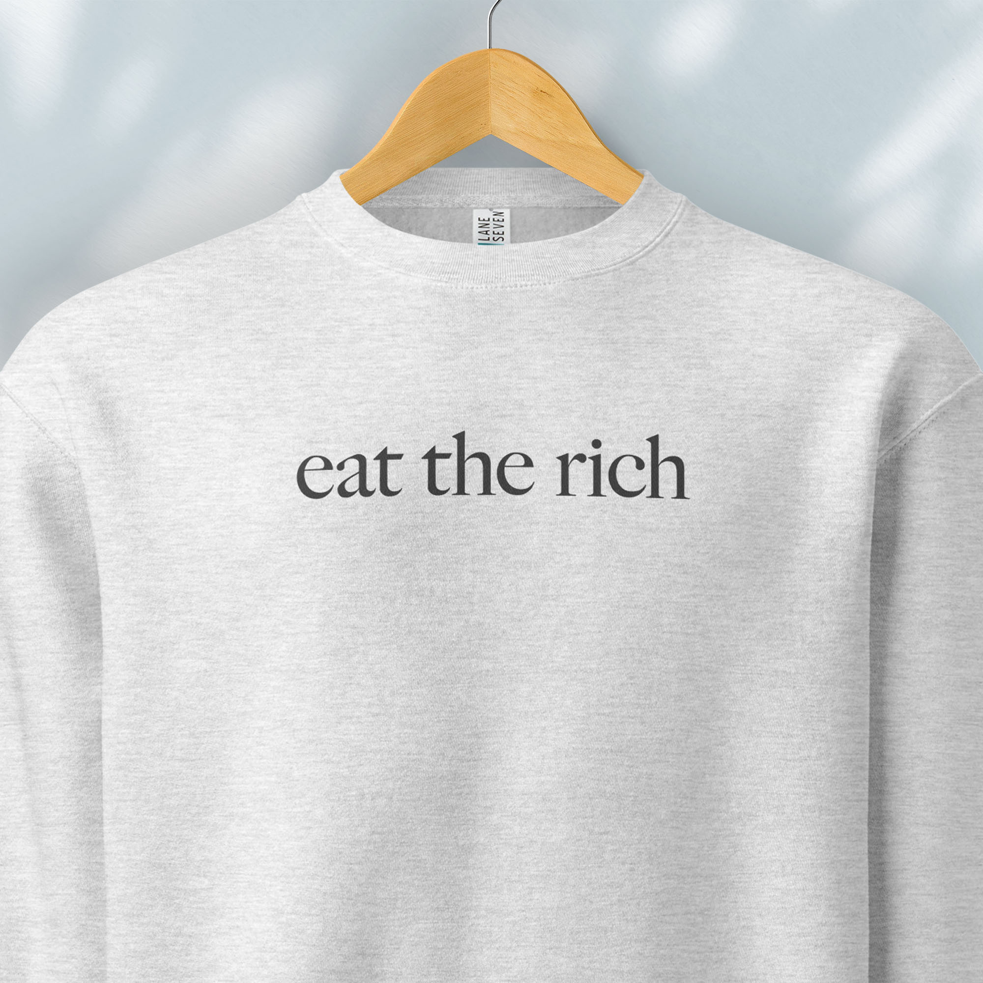 Hanging heather grey sweatshirt with minimalist dark grey text reading “eat the rich."
