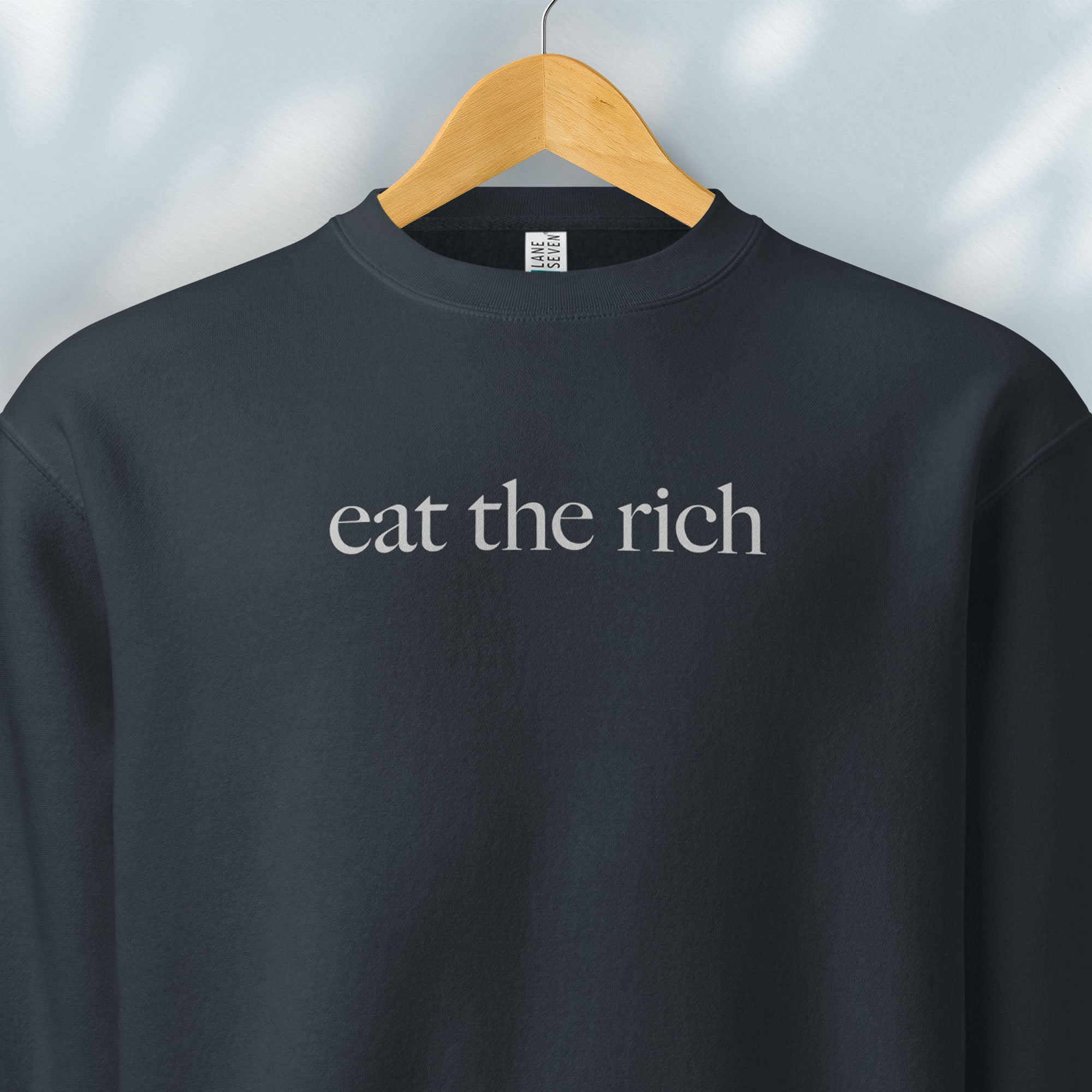 Hanging navy sweatshirt with minimalist light grey text reading “eat the rich."
