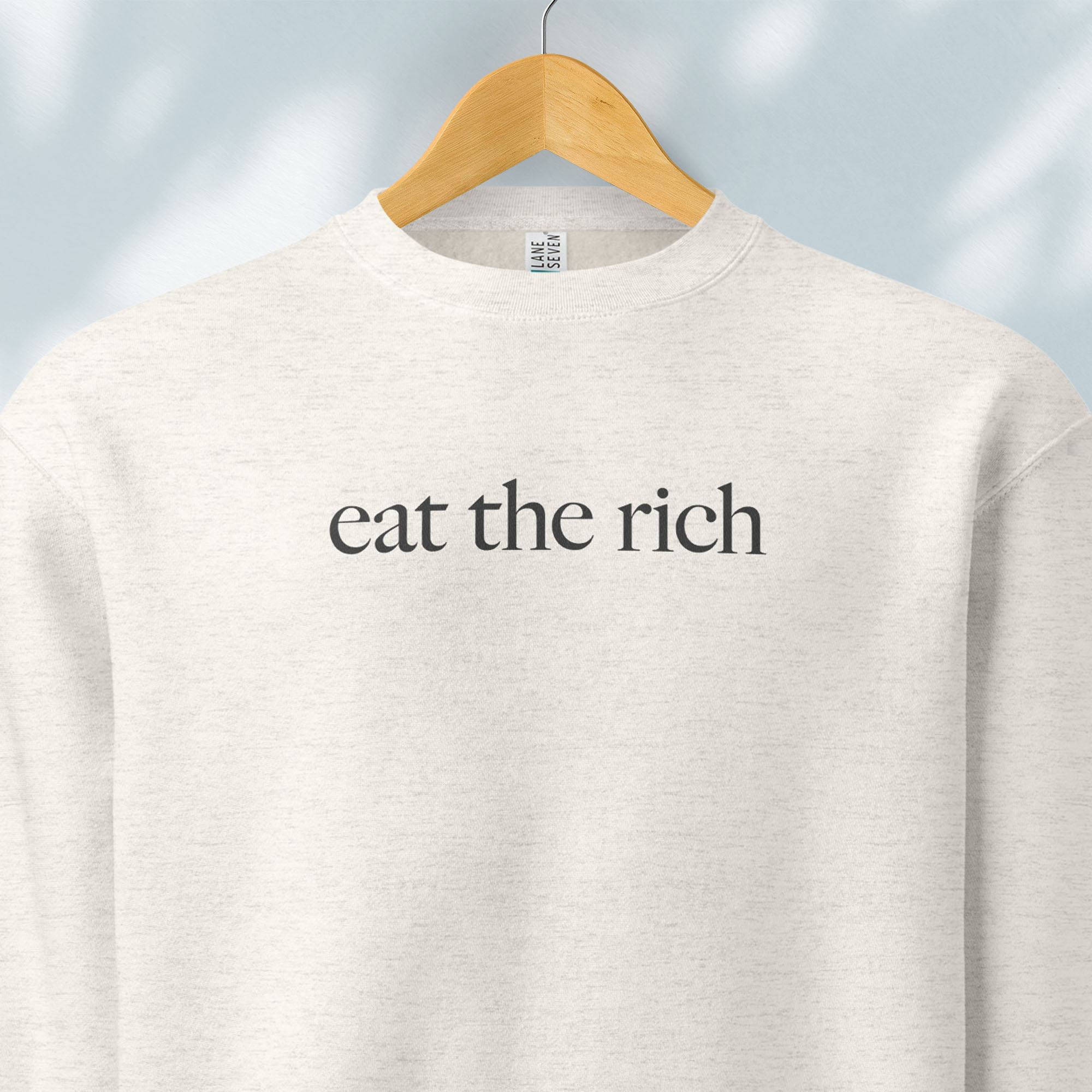 Hanging oatmeal heather sweatshirt with minimalist dark grey text reading “eat the rich."