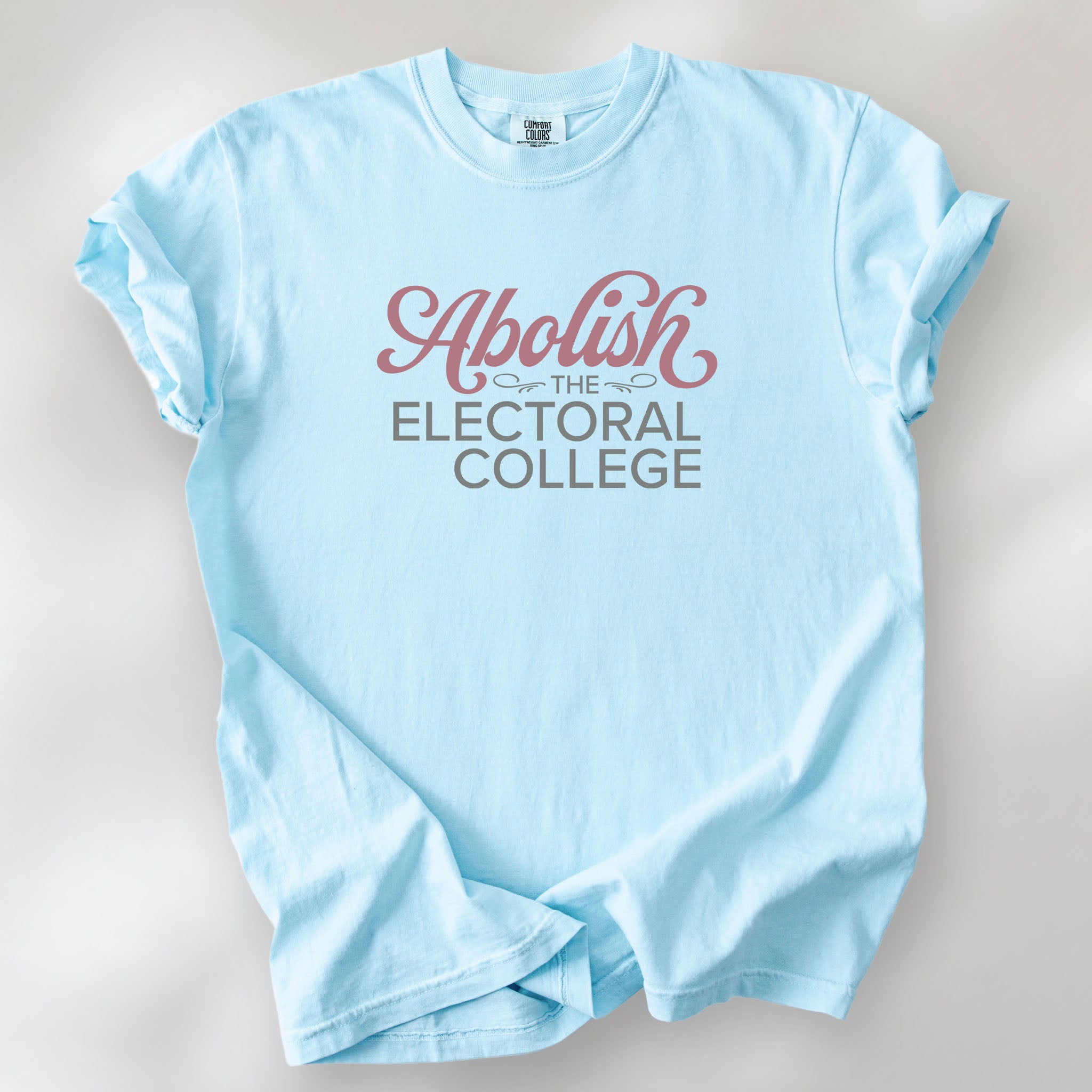 Chambray t-shirt with stylized text reading “Abolish the Electoral College” in muted red and gray, minimalist pro-democracy design.