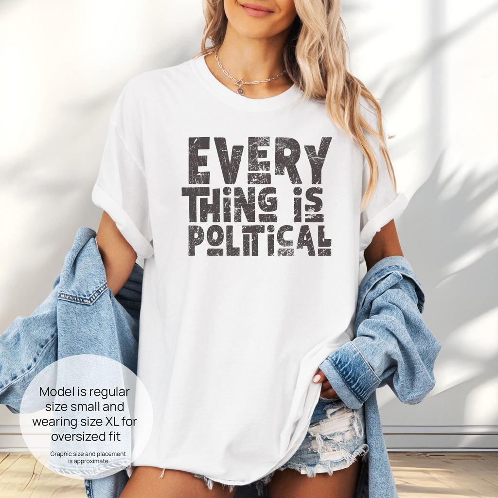 Female model wearing oversized white t-shirt featuring distressed block typography reading "Everything Is Political" in a bold minimalist design. Includes size and fit information for the model who is regular size small, and wearing a size XL shirt for an oversized fit.
