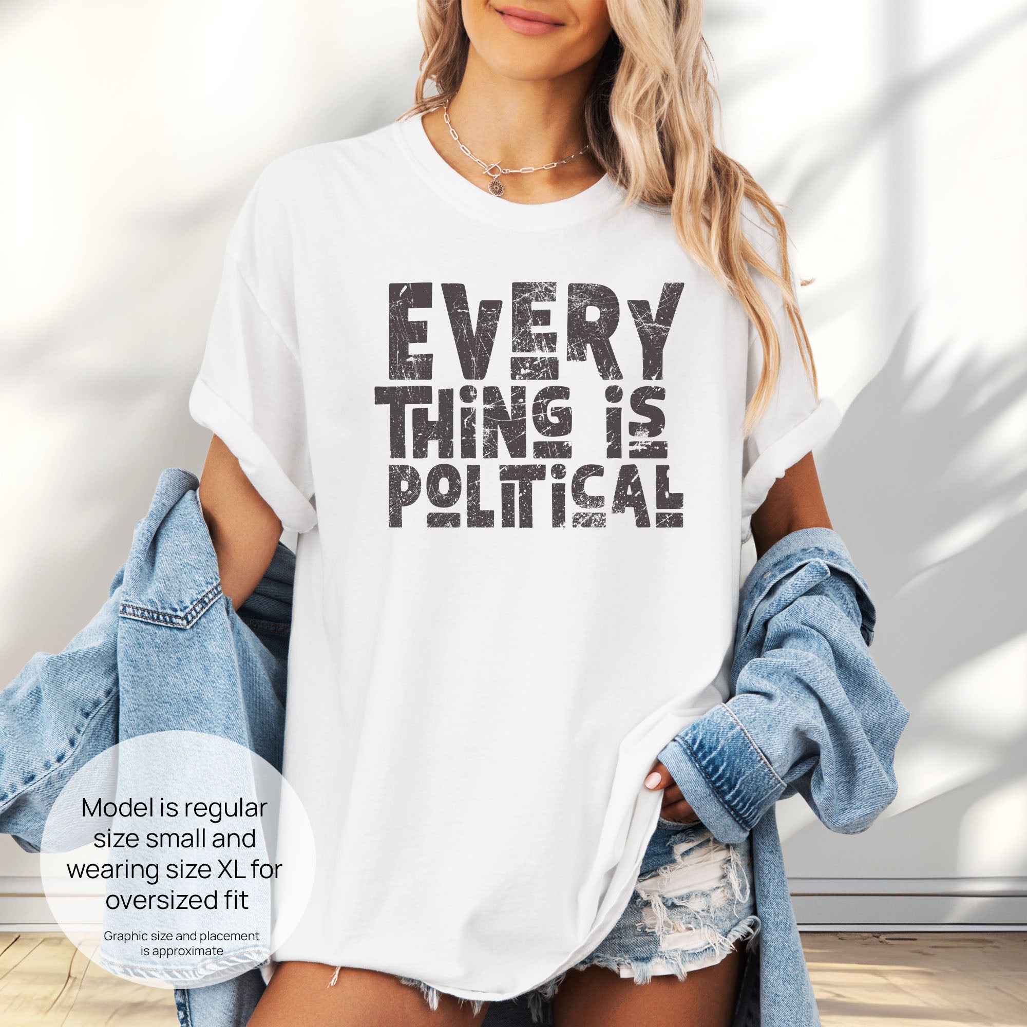 Female model wearing oversized white t-shirt featuring distressed block typography reading "Everything Is Political" in a bold minimalist design. Includes size and fit information for the model who is regular size small, and wearing a size XL shirt for an oversized fit.
