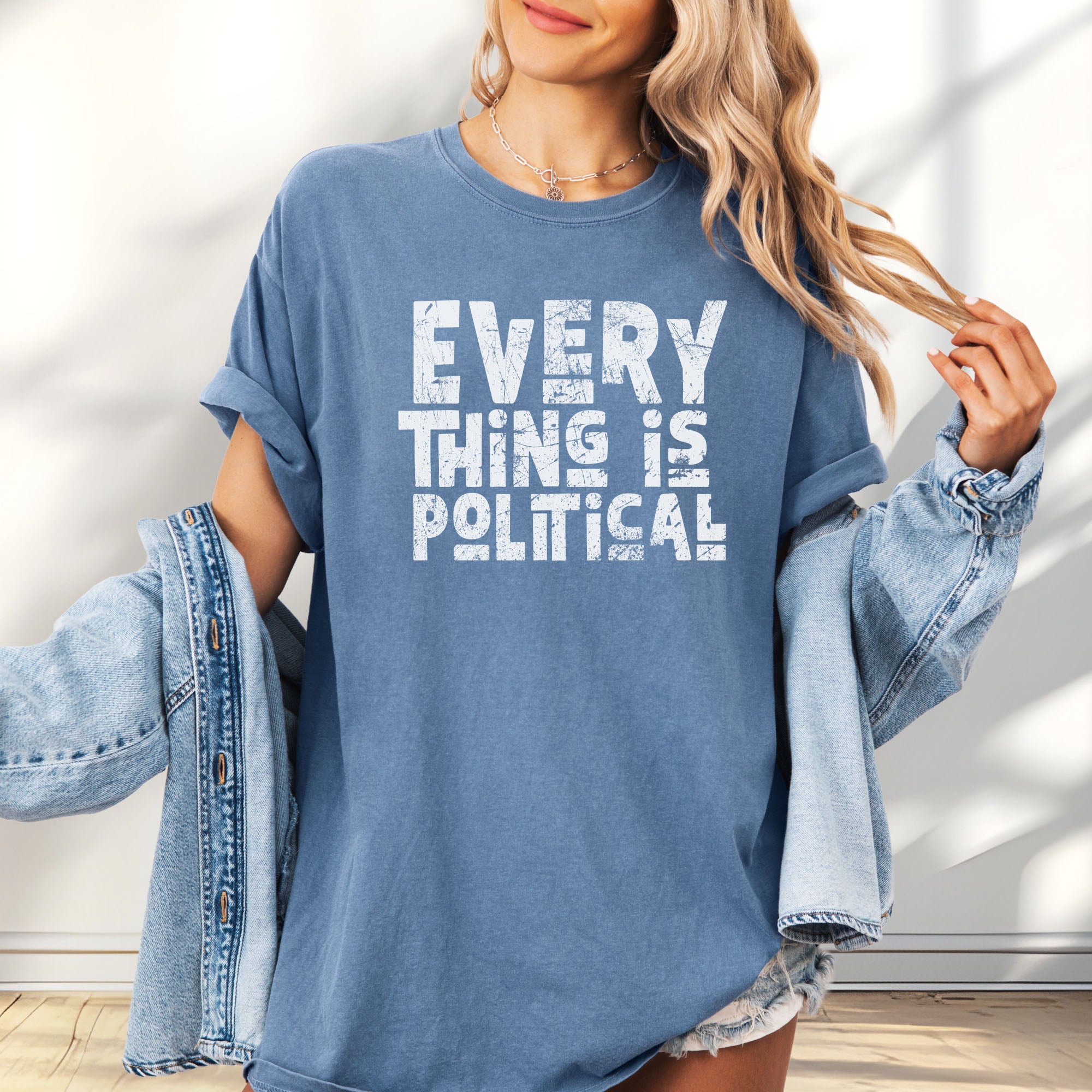 Female model wearing oversized blue jean t-shirt featuring distressed block typography reading "Everything Is Political" in a bold minimalist design.