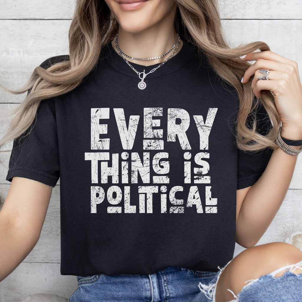 Female model wearing black t-shirt featuring distressed block typography reading "Everything Is Political" in a bold minimalist design.