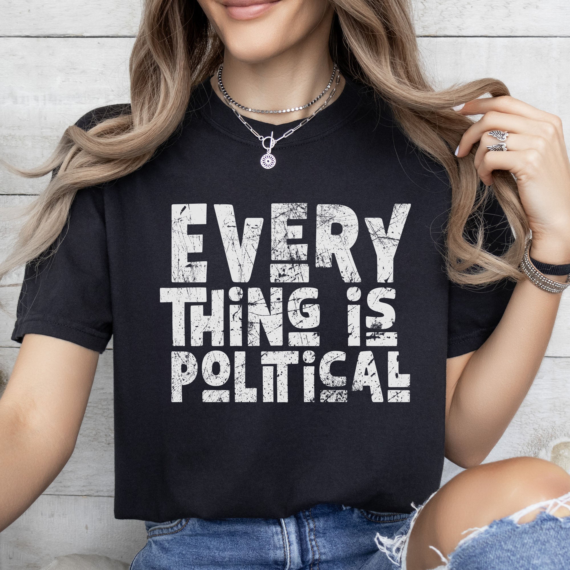 Female model wearing black t-shirt featuring distressed block typography reading "Everything Is Political" in a bold minimalist design.