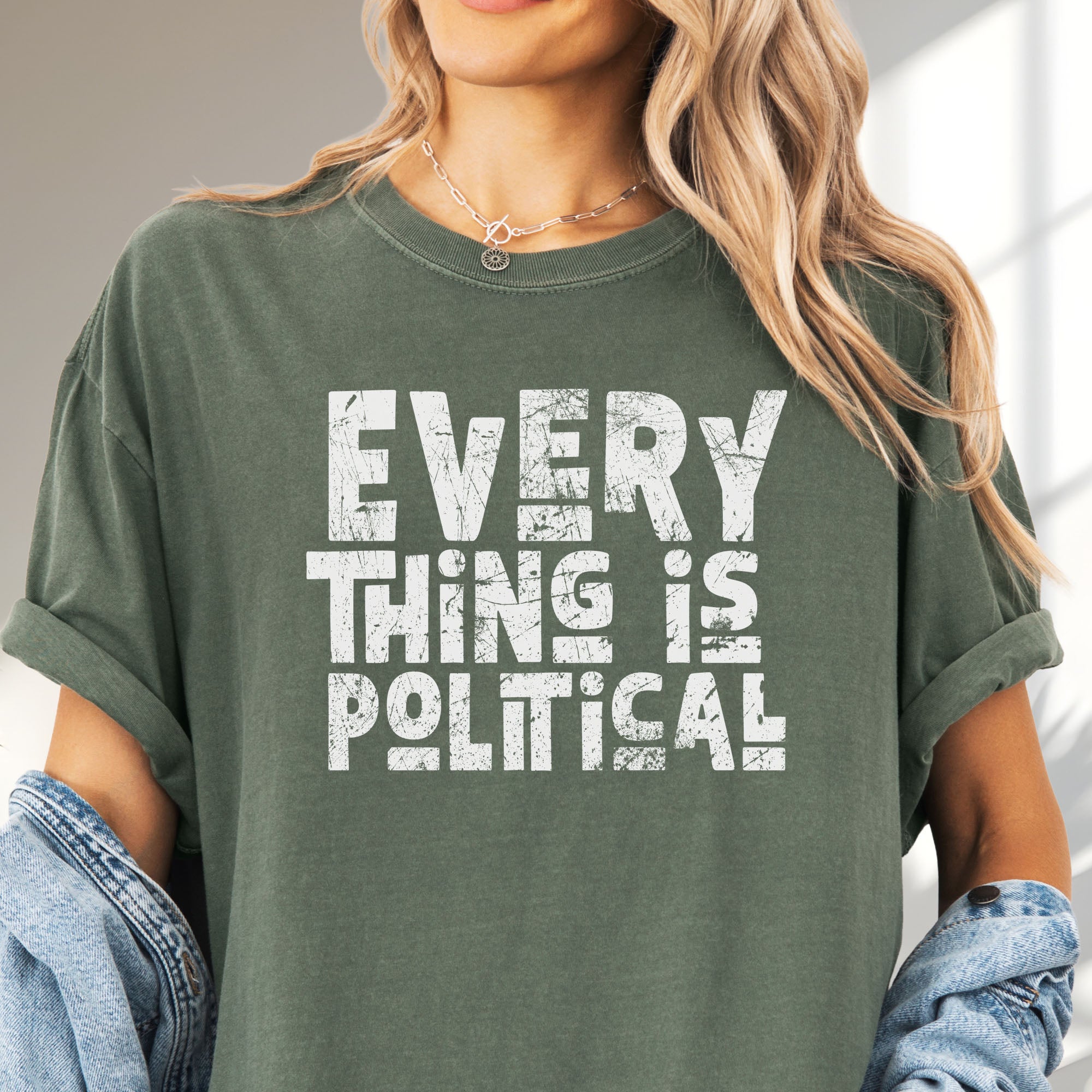Female model wearing oversized moss t-shirt featuring distressed block typography reading "Everything Is Political" in a bold minimalist design.