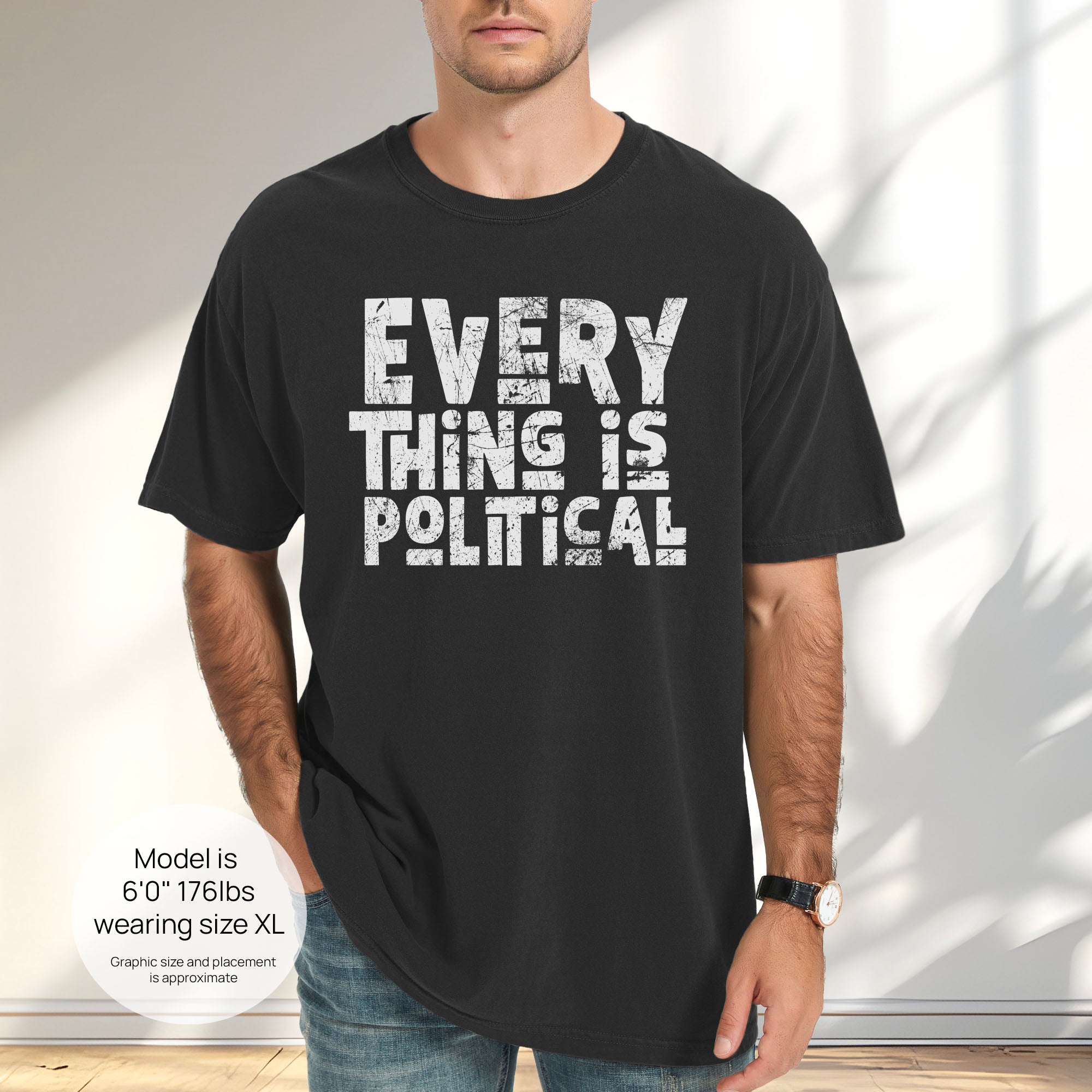 Male model wearing black t-shirt featuring distressed block typography reading "Everything Is Political" in a bold minimalist design. Includes size and fit information for the model who is 6 feet 0 inches, 176 pounds, and wearing a size XL shirt.
