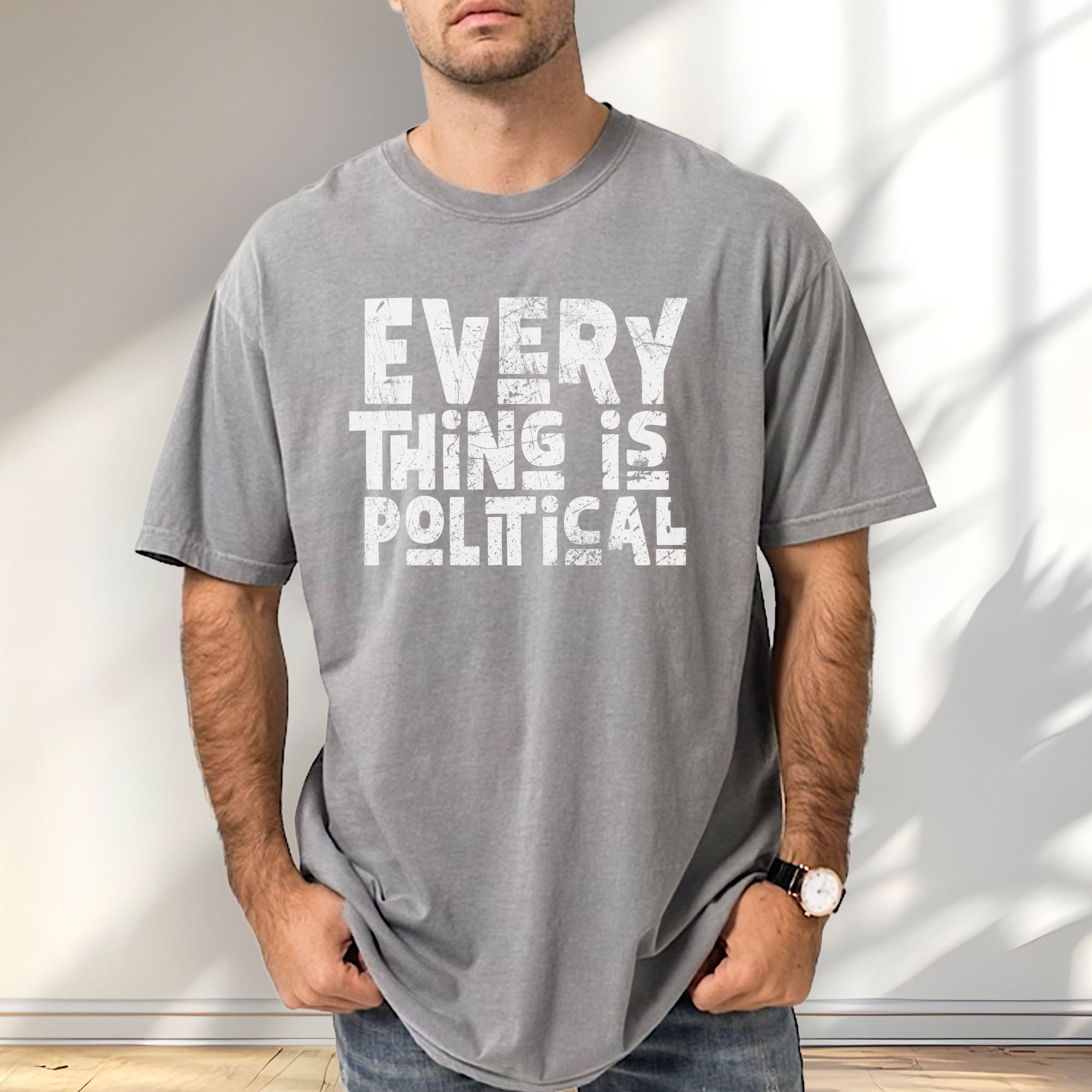 Male model wearing grey t-shirt featuring distressed block typography reading "Everything Is Political" in a bold minimalist design.