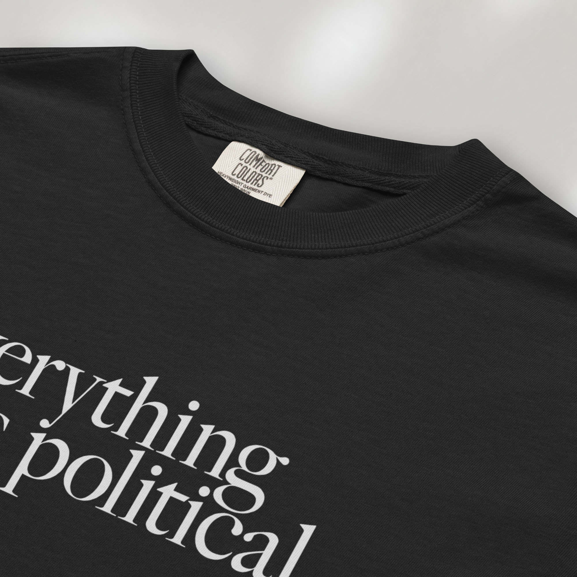 Closeup detail of black unisex t-shirt with minimalist serif gray text reading “everything is political."
