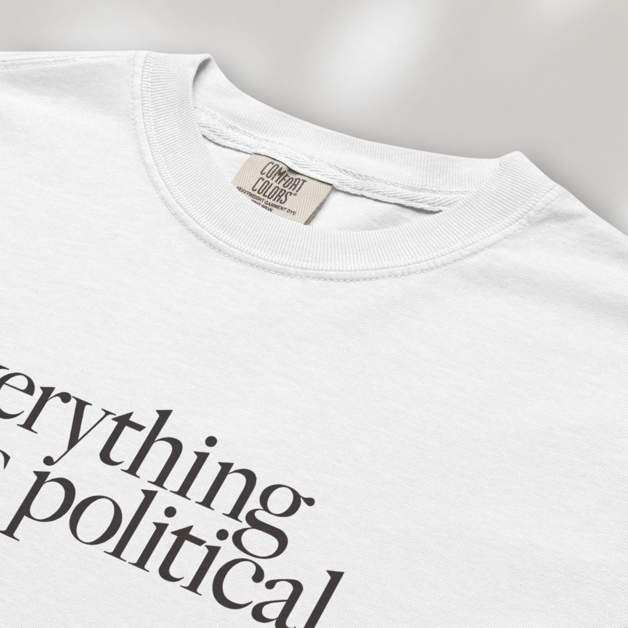 Closeup detail of white unisex t-shirt with minimalist serif gray text reading “everything is political."
