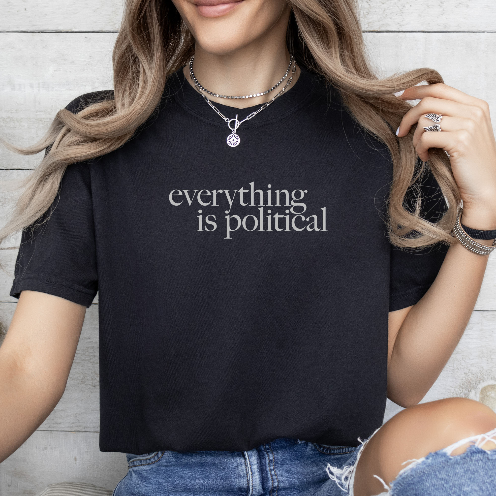 Female model wearing black unisex t-shirt with minimalist serif gray text reading “everything is political.