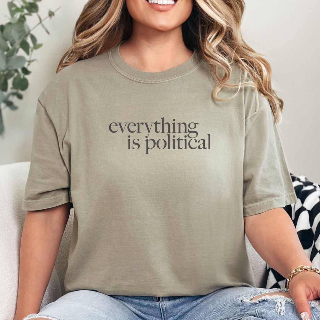 Female model wearing khaki unisex t-shirt with minimalist serif gray text reading “everything is political."