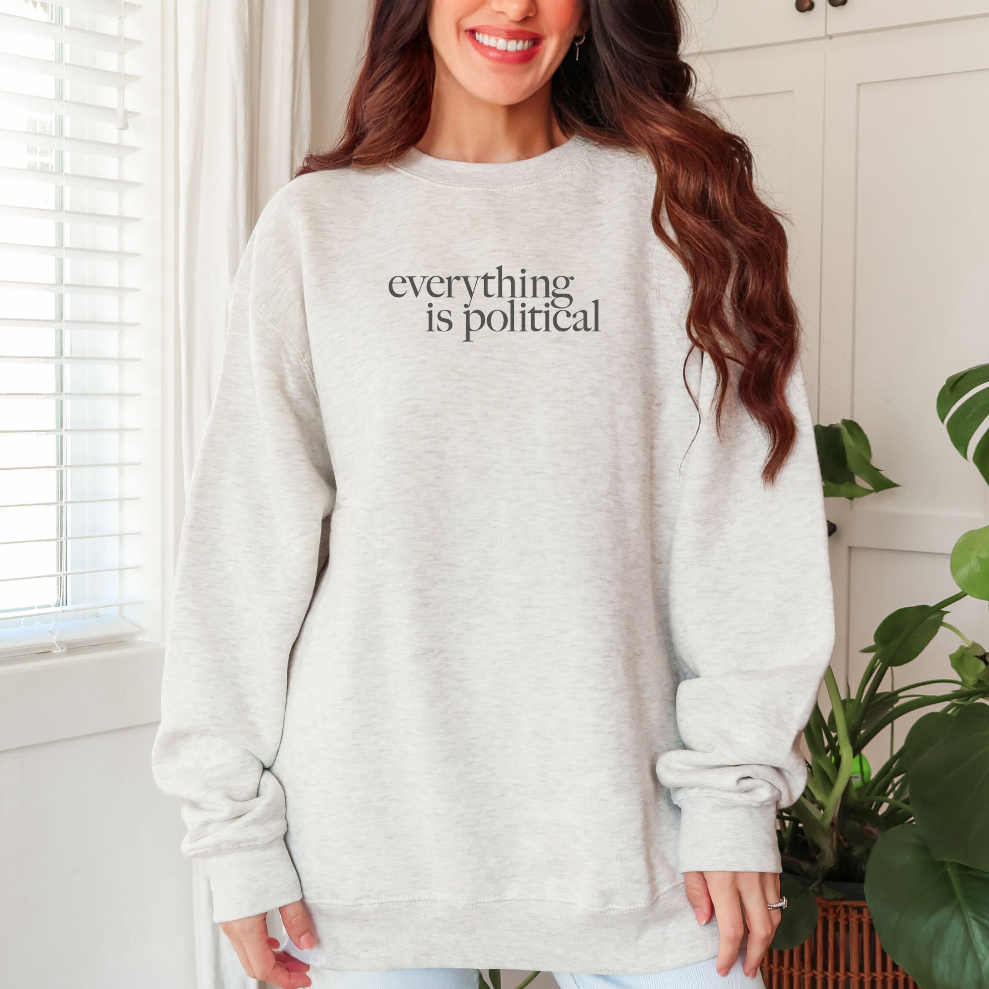 Female model wearing oversized oatmeal sweatshirt with minimalist serif gray text reading “everything is political."
