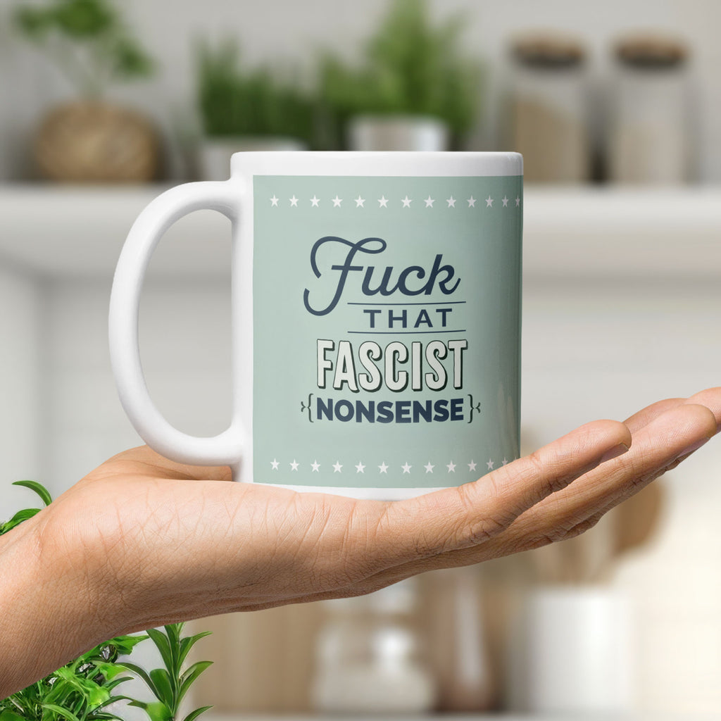 Ceramic mug with graphic on mint green background and navy styled text block that reads "fuck that fascist nonsense." Mug is resting in the palm of a hand.