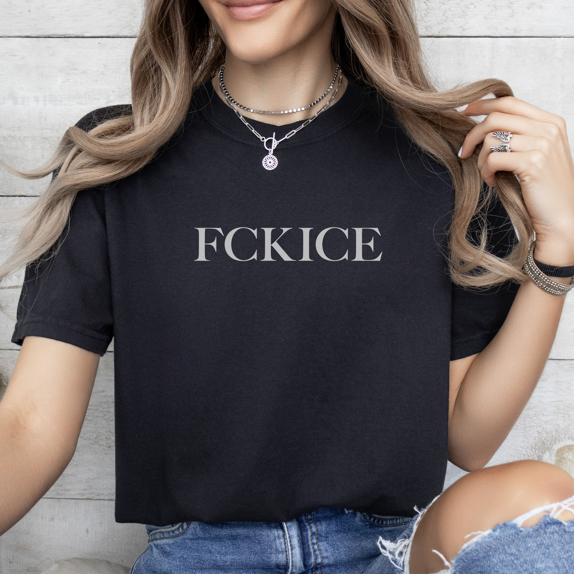 Female model wearing black unisex t-shirt with minimalist serif typography reading “FCK ICE,” an anti-ICE political message opposing Immigration and Customs Enforcement abuses and violence.