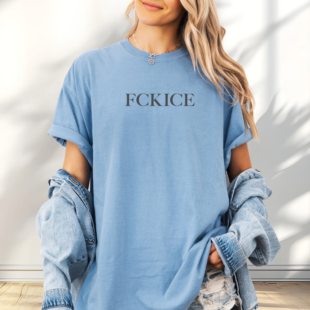 Female model wearing oversized washed denim unisex t-shirt with minimalist serif typography reading “FCK ICE,” an anti-ICE political message opposing Immigration and Customs Enforcement abuses and violence.
