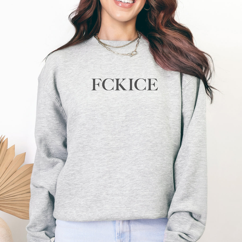 Female model wearing heather grey unisex sweatshirt with minimalist serif typography reading “FCK ICE,” an anti-ICE political message opposing Immigration and Customs Enforcement abuses and violence.