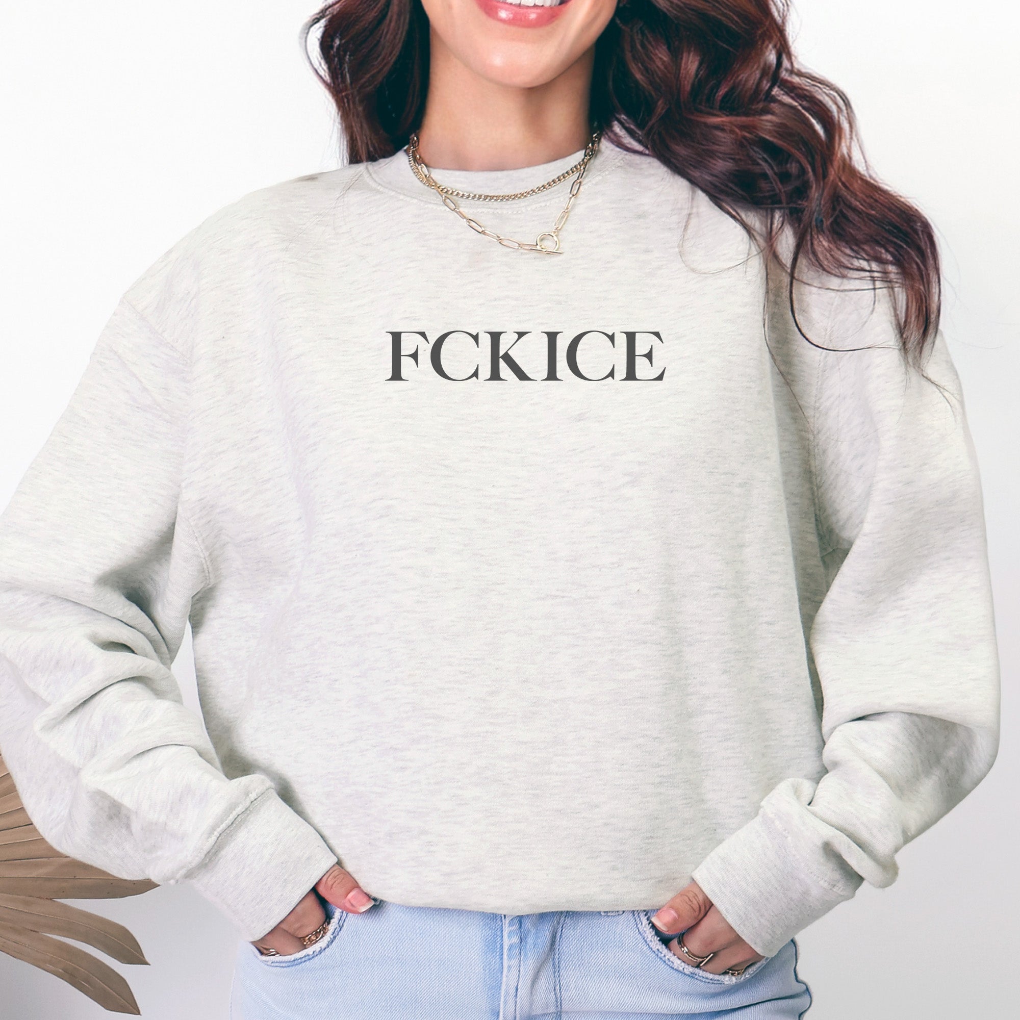 Female model wearing oatmeal unisex sweatshirt with minimalist serif typography reading “FCK ICE,” an anti-ICE political message opposing Immigration and Customs Enforcement abuses and violence.
